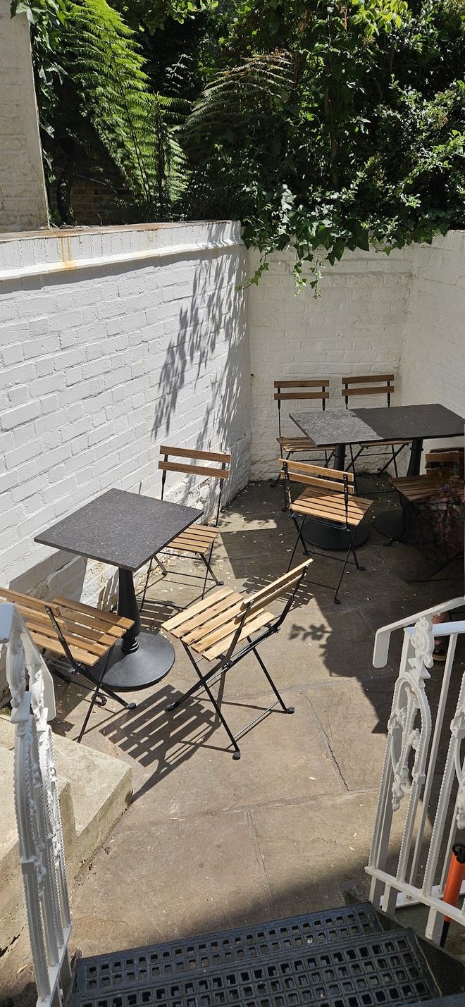The sunlit back terrace with folding bistro tables against a white brick wall under greenery.