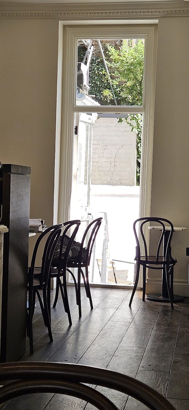 An interior corner with bentwood chairs and dark floorboards looking out through a bright doorway.