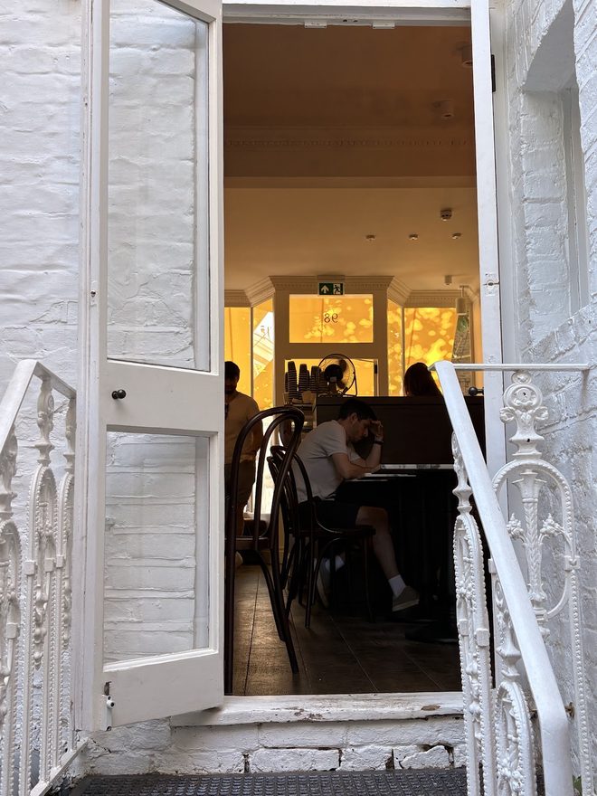 The white front door and railings seen from the street steps, the room warm-lit inside.