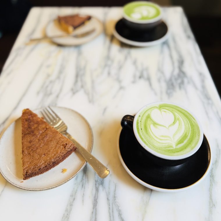 A slice of tart on a plate with a matcha latte alongside.